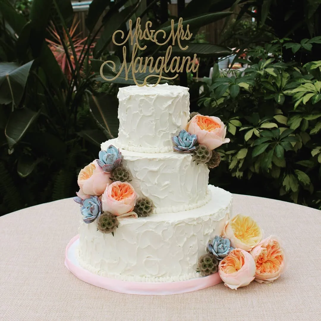A tall floral wedding cake set up outdoors by AMR Catering, decorated with fresh blooms.