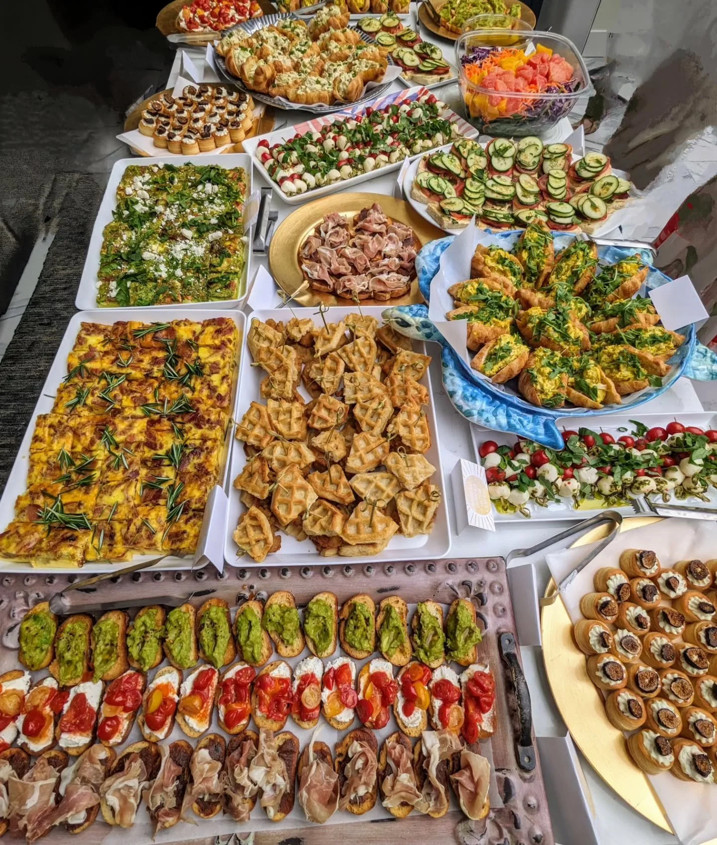 An overhead savory grazing spread by AMR Catering with bruschetta, caprese, frittata and prosciutto arranged generously across a table.