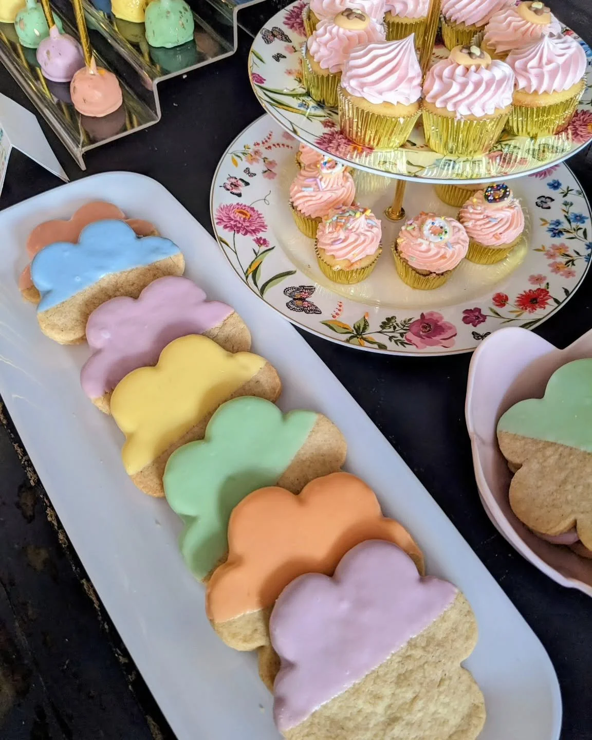 A tray of rainbow cupcakes by AMR Catering, each piped with a different colorful frosting swirl.